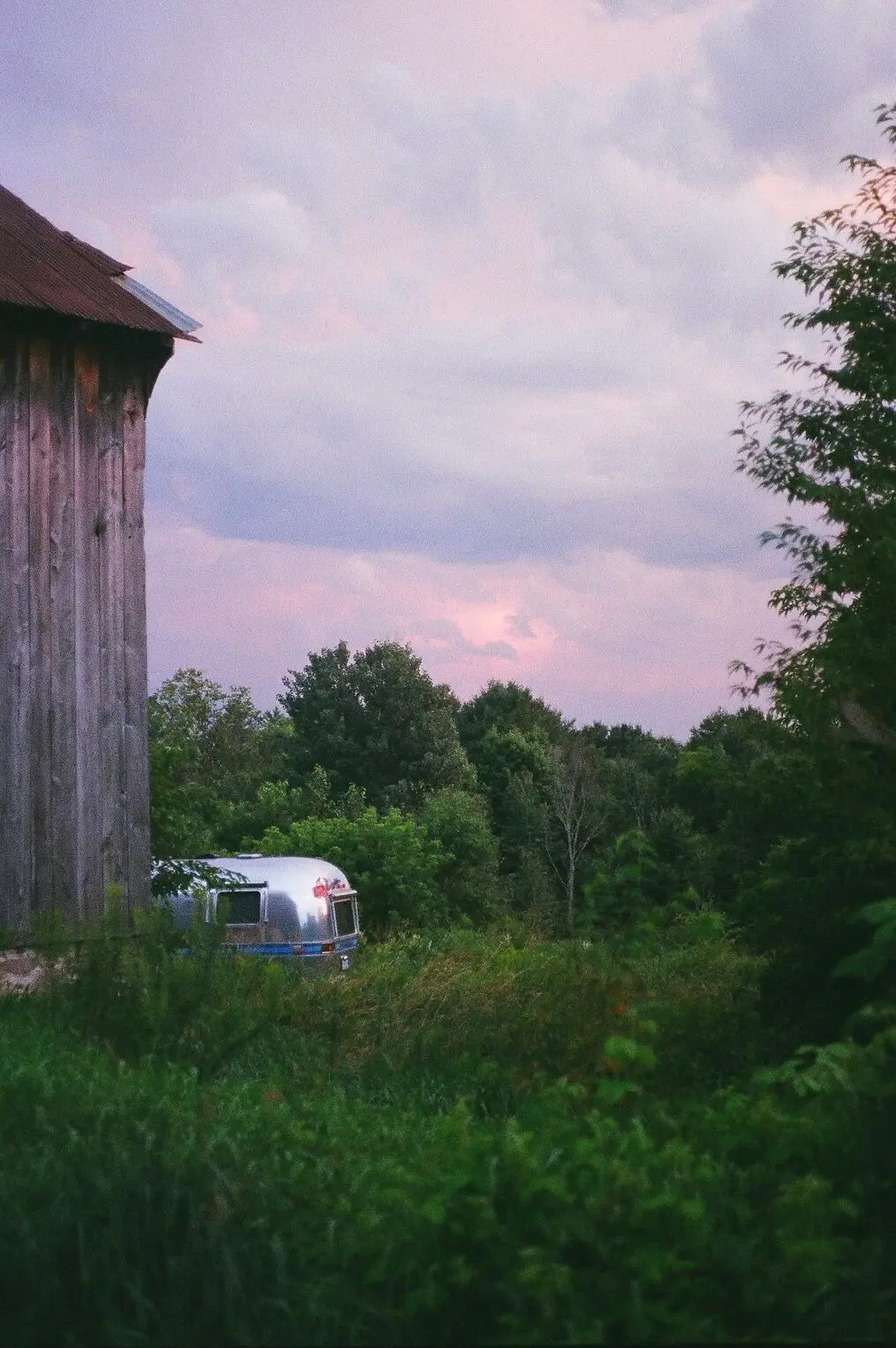 The barn silo and Airstream silhouetted against a pink and lilac sunset