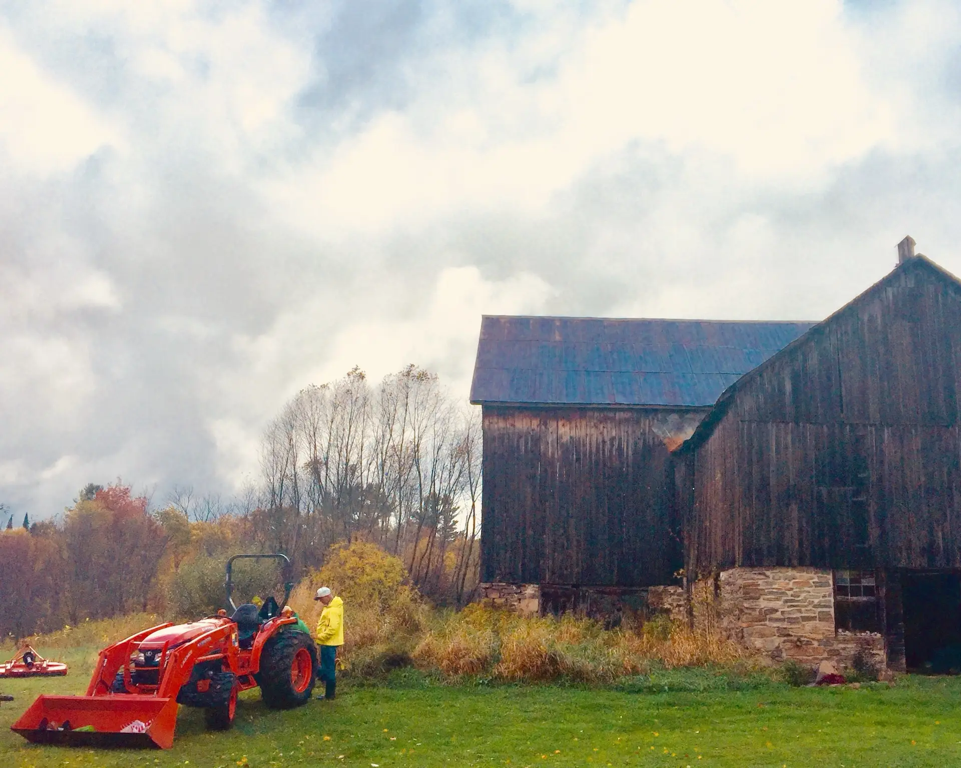A red tractor parked beside the weathered timber barn, with bonfire smoke drifting across an autumn sky